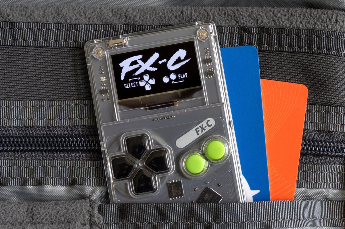 The Arduboy FX-C handheld console is shown from the front, highlighting its credit card size and monochromatic screen.