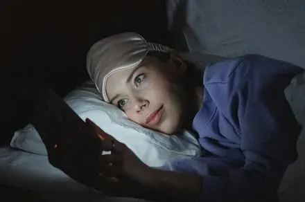 Young adults using smartphones in bed at night, illustrating the link between screen time and sleep disruption.