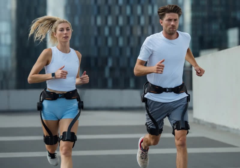 The device features a waist belt connected to hinged thigh braces and carbon-fiber linkages powered by hip-mounted motors.