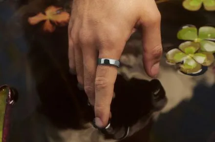 The titanium Oura Ring 5 smart ring sits beside its aluminum charging case.