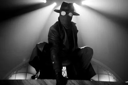 Ben Reilly stands in a trench coat and fedora against a shadowy cityscape in black and white.