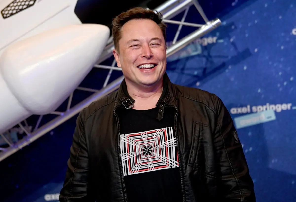 Elon Musk stands behind the monologue desk during his Saturday Night Live hosting appearance.