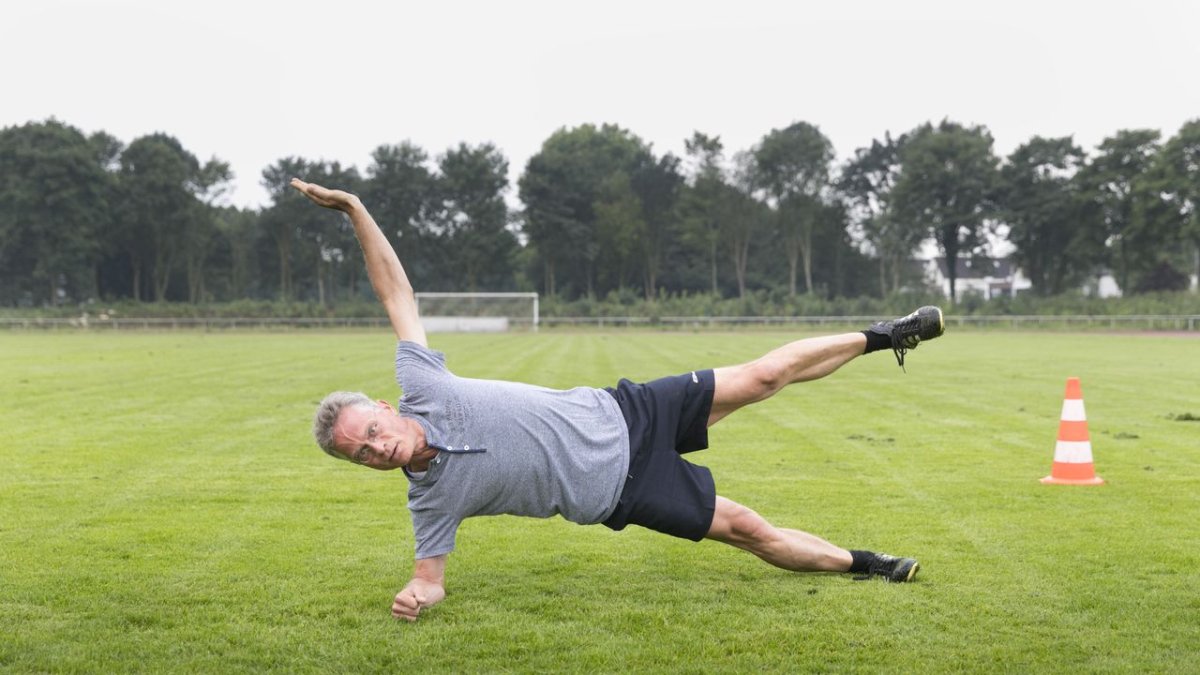 Older adults perform gentle bodyweight exercises while reviewing a digital training plan on a tablet.