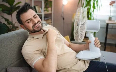 Standing fan positioned facing an open window to create negative pressure ventilation for home cooling.