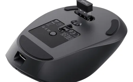 A Trust Zevo rechargeable multi-wireless mouse rests on a desk next to its wireless receiver and charging cable.