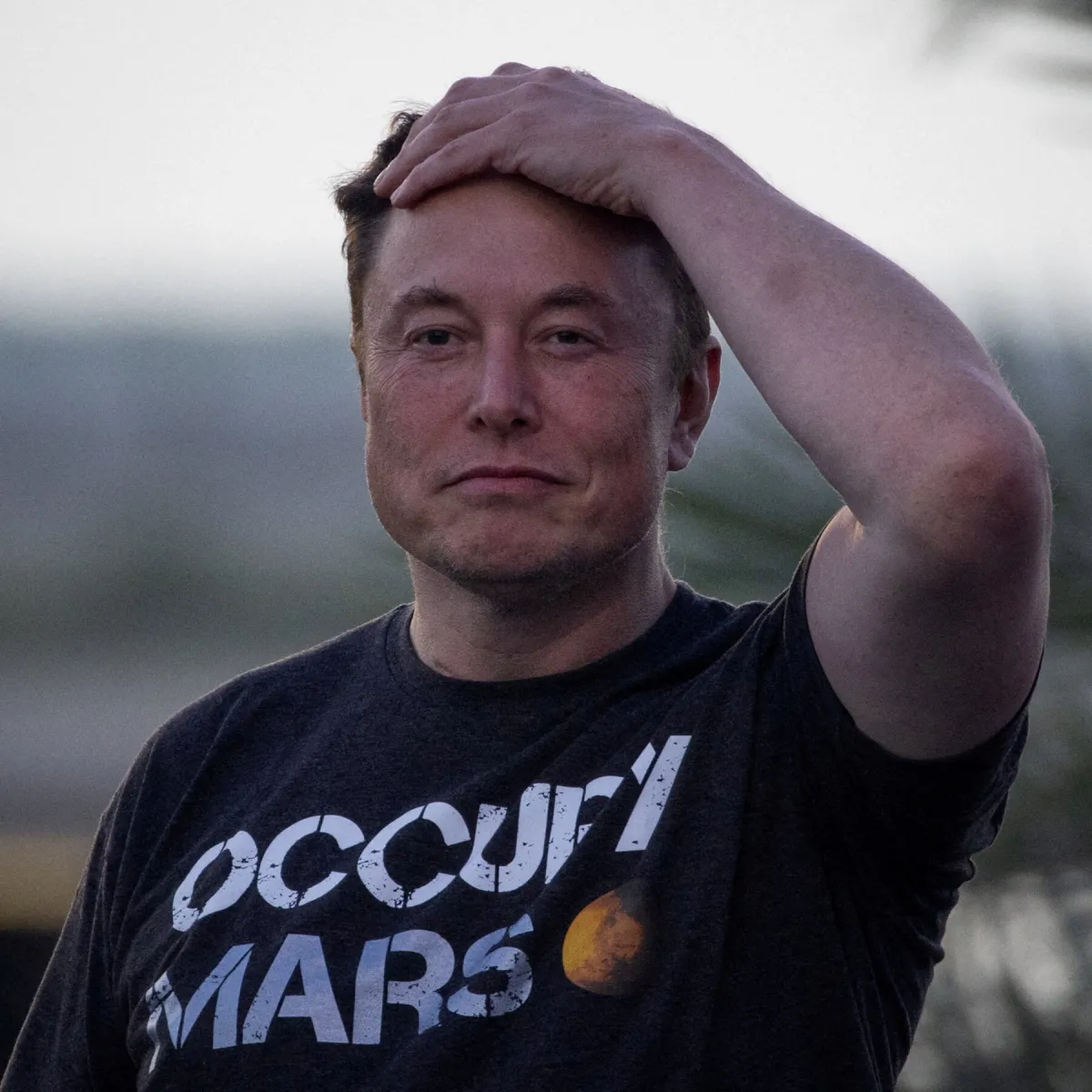 Elon Musk stands beside a financial chart marking his net worth crossing one trillion dollars.