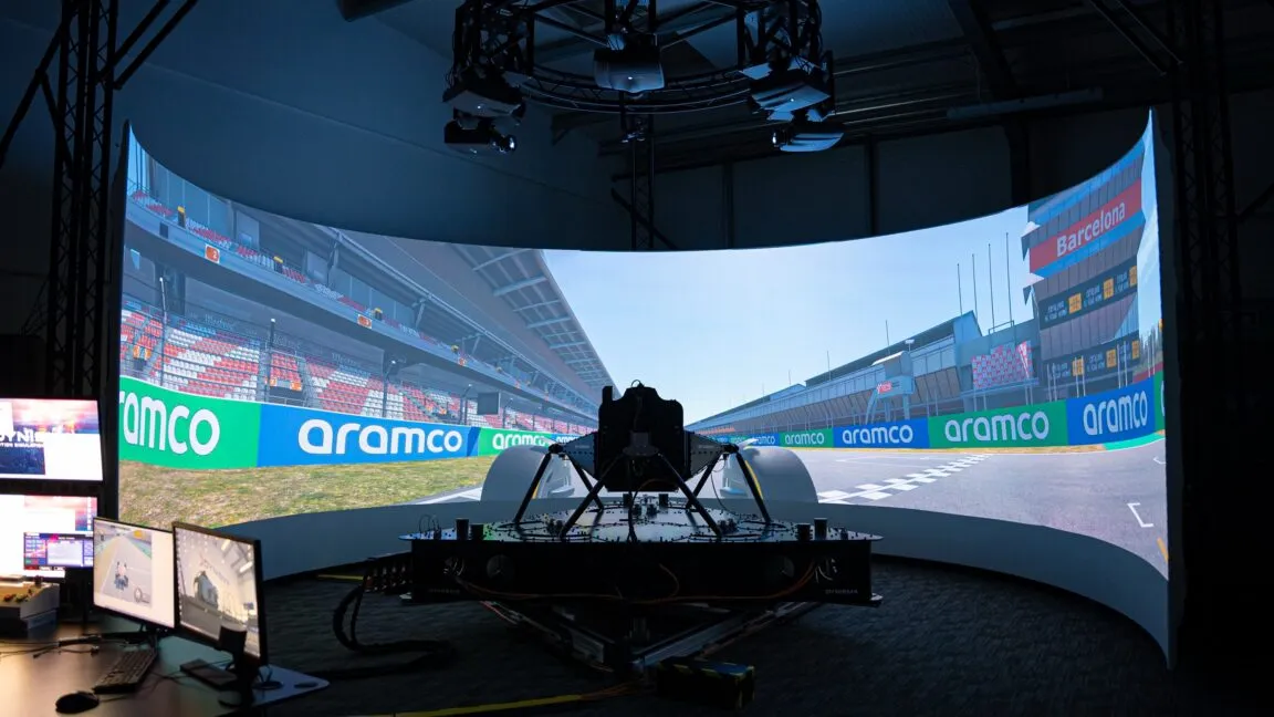 Formula 1 simulator cockpit with a motion platform, steering wheel, and screens for driver training and engineering analysis.