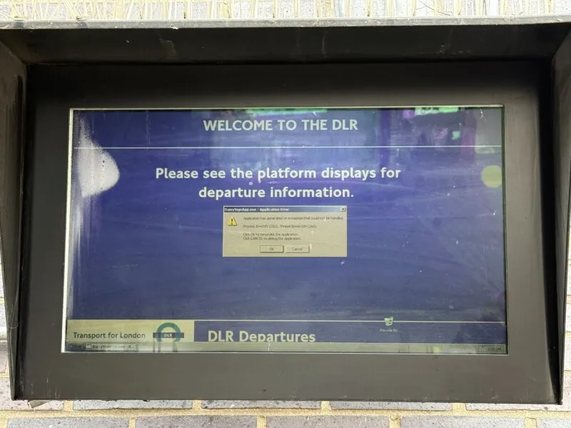 A vintage Windows error message appears on a Docklands Light Railway information screen at Limehouse station.