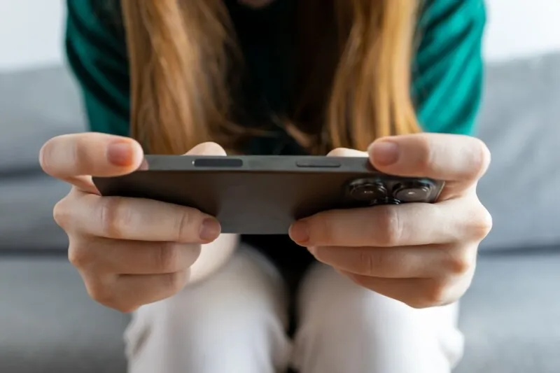 A teenager holds a smartphone next to a digital clock showing proposed UK social media age limits.