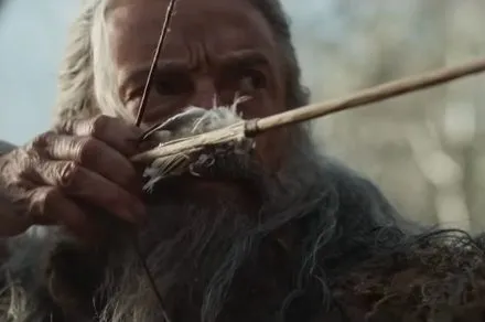 A weathered archer stands in a quiet landscape, reflecting the film's exploration of guilt and redemption.