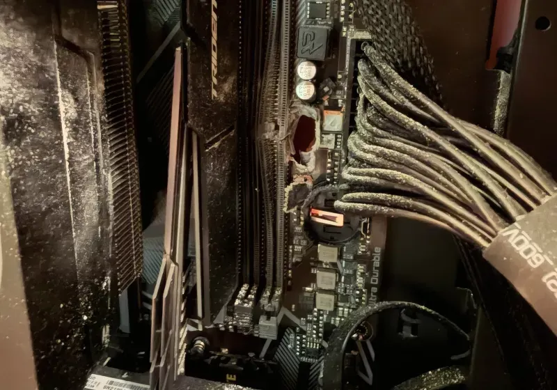 A damaged gaming PC displays a bullet hole in the chassis with a deflected round near the RAM module.