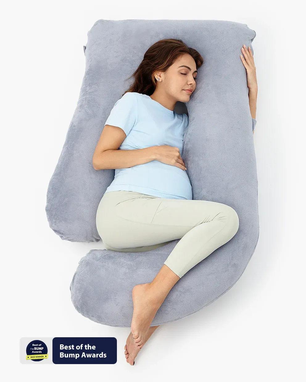 A pregnant woman sleeps on her side while using a curved maternity pillow for ergonomic support.