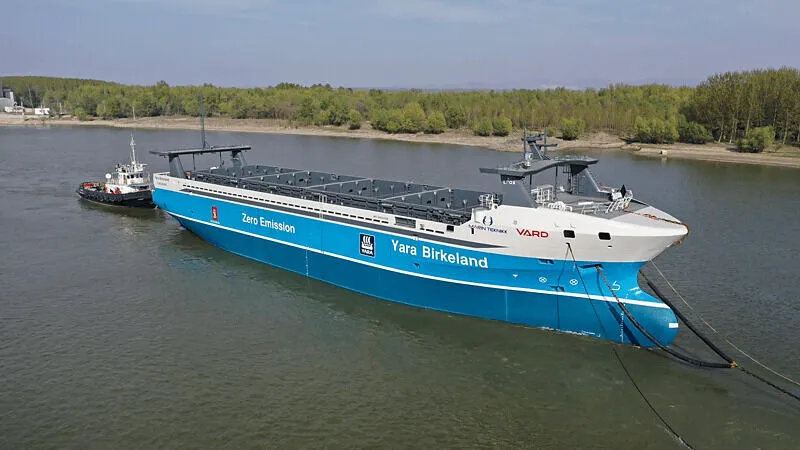 An autonomous cargo ship navigates open waters while maritime regulators draft safety guidelines.