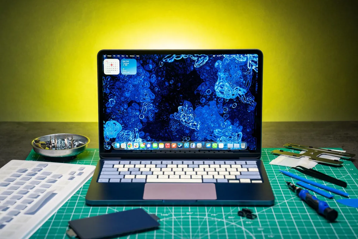 A MacBook Neo laptop displays removable color panels and modular internal components arranged for user assembly.