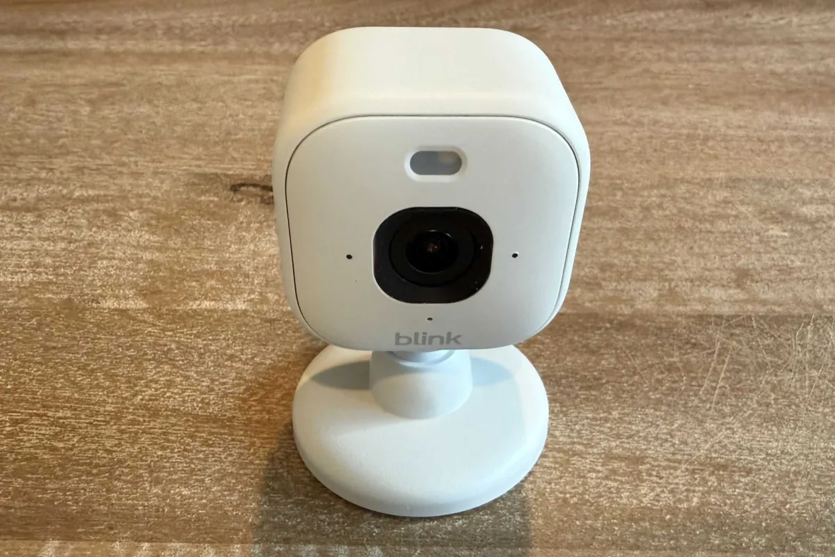 Three Blink Mini 2K+ security cameras are arranged on a table with power adapters and mounting brackets.