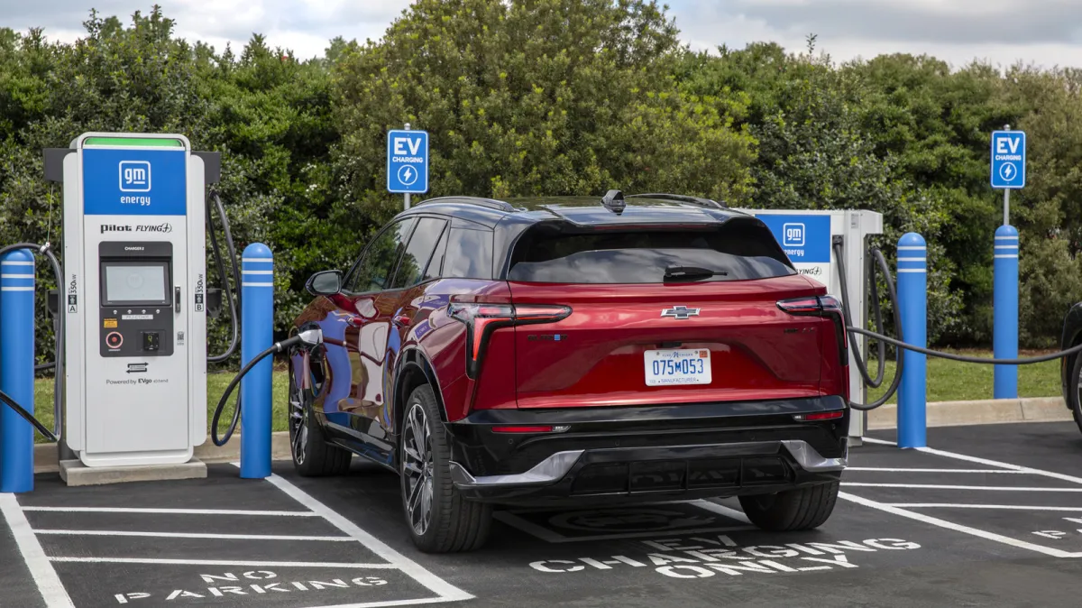 A General Motors electric vehicle connects to a public charging station while demonstrating vehicle-to-grid power transfer.