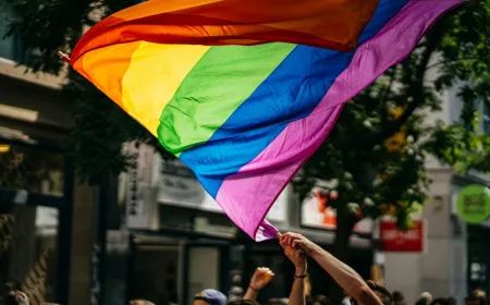 Crowd waving rainbow flags and holding signs at a Pride march.