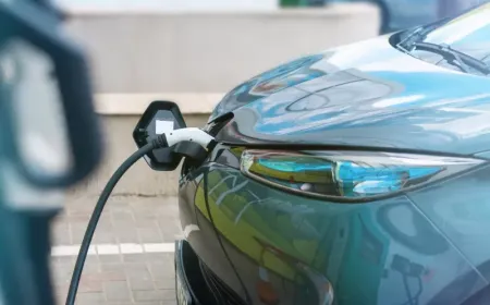 Electric vehicle at a public charging station with visible payment terminal and access restriction signage.