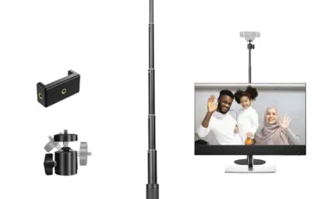 A webcam is mounted on a monitor frame next to a ring light and desktop microphone.