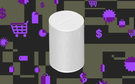 The Sonos Era 100 compact smart speaker sits on a wooden surface.