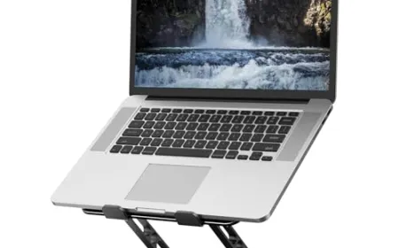MacBook on a raised stand with external keyboard, mouse, and adjustable desk lamp