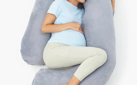 A pregnant woman sleeps on her side while using a curved maternity pillow for ergonomic support.