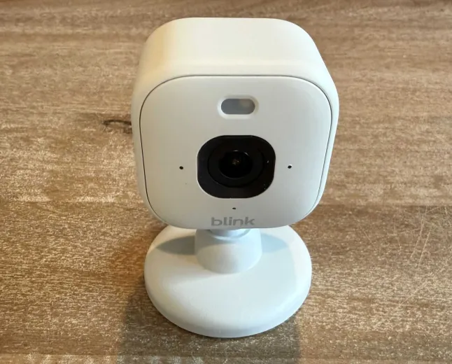 Three Blink Mini 2K+ security cameras are arranged on a table with power adapters and mounting brackets.